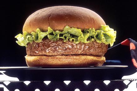 A hamburger with a rim of lettuce sitting on a black plate against a black background with a black and red napkin on a black and white-dotted tablecloth
