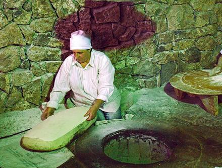 Tonir, gdzie tradycyjnie wypieka się lawasz. Kobieta rozkłada właśnie placek na formie w kształcie poduszki.